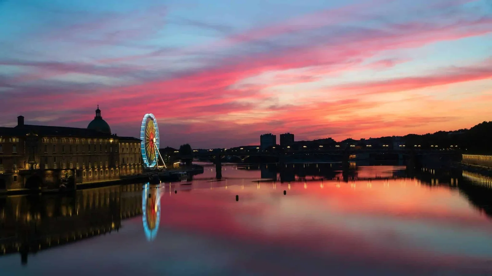 Waterkant van Toulouse bij zonsondergang met een reuzenrad en gebouw met koepel