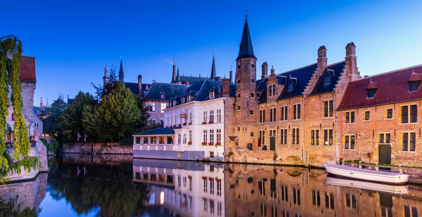 Uitzicht op een gracht in Brugge met het belfort bij schemering