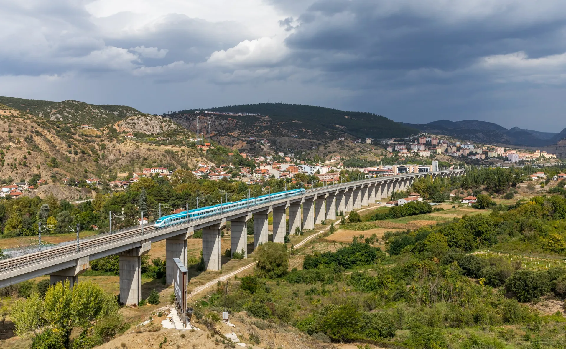 Ein weiß-türkiser Hochgeschwindigkeitszug der Baureihe HT80000 von TCDD Taşımacılık überquert das lange Betonviadukt über der Stadt Bilecik im Nordwesten der Türkei.