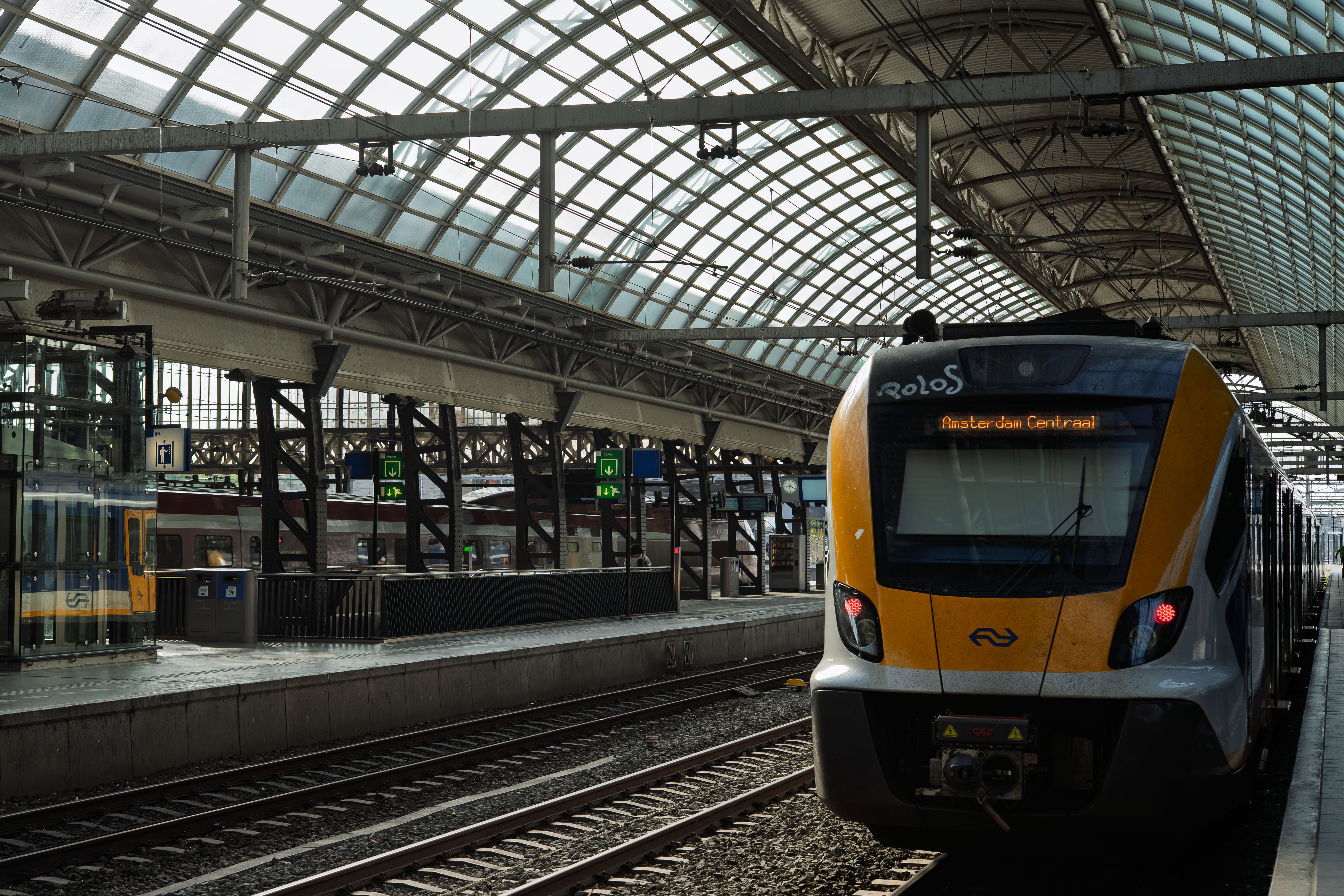Een gele NS-trein op Amsterdam Centraal onder het glazen dak van het station