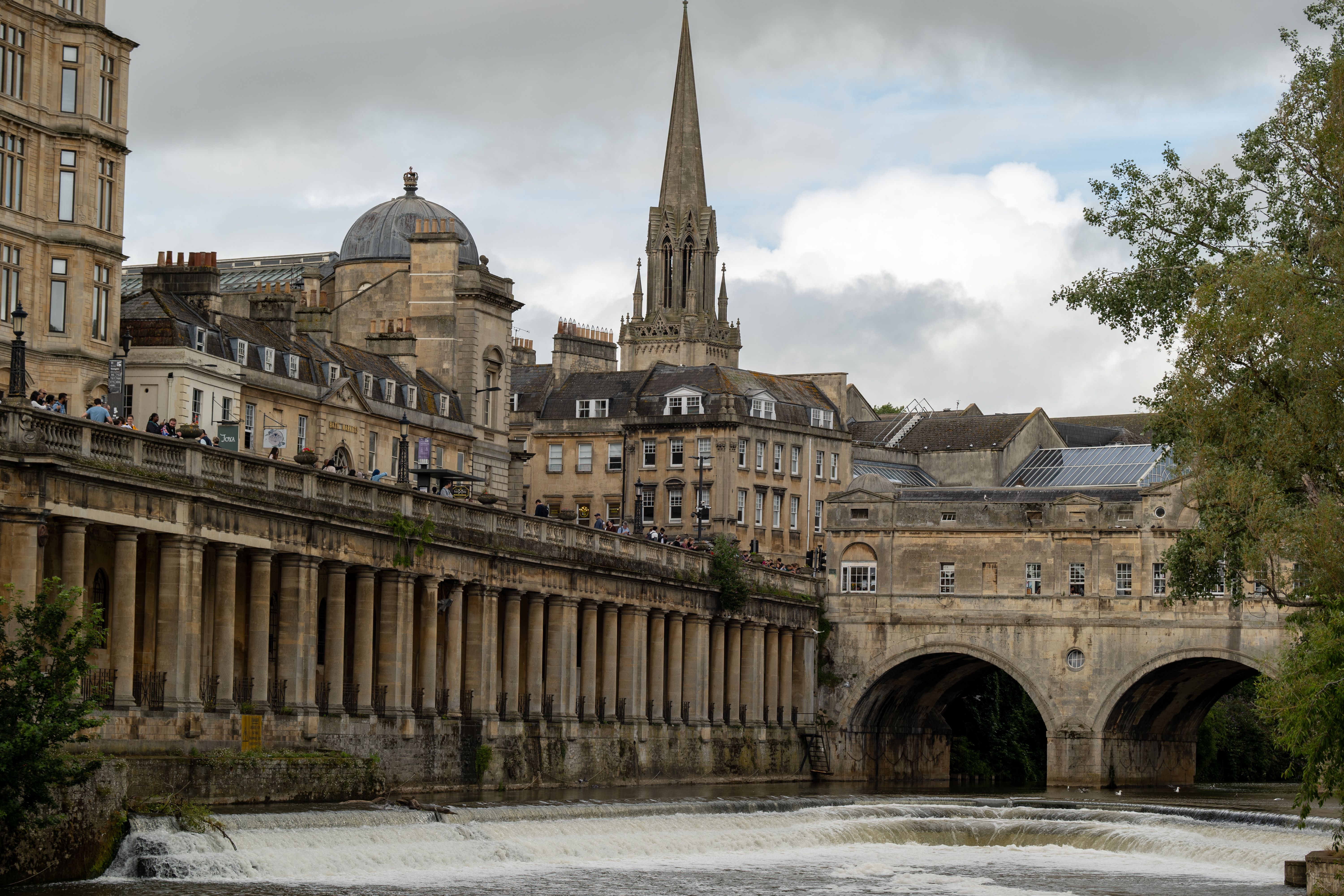 Pulteney Bridge och överfallsdammen i floden Avon i Bath, med den georgianska kolonnaden och ett kyrktorn bakom