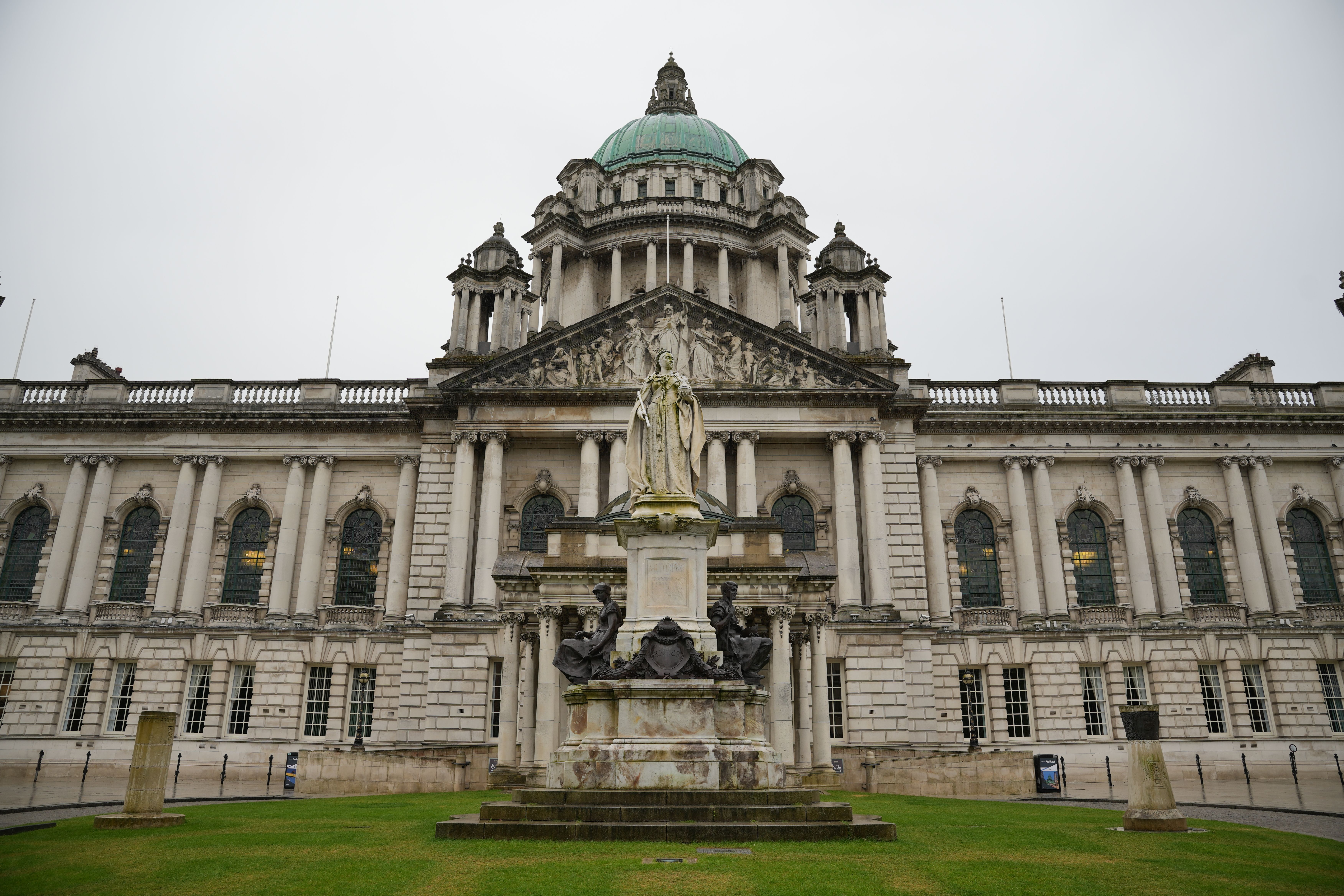 Front facade of Belfast City Hall with its green copper dome and the Queen Victoria memorial statue on the lawn