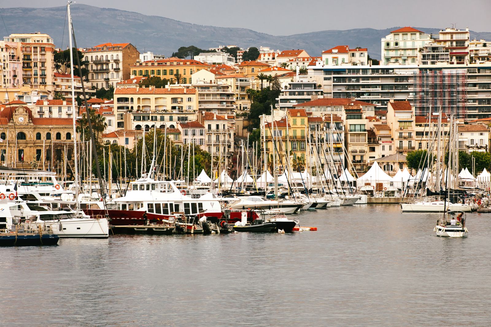Cannes harbour filled with yachts, waterfront buildings and hills behind.