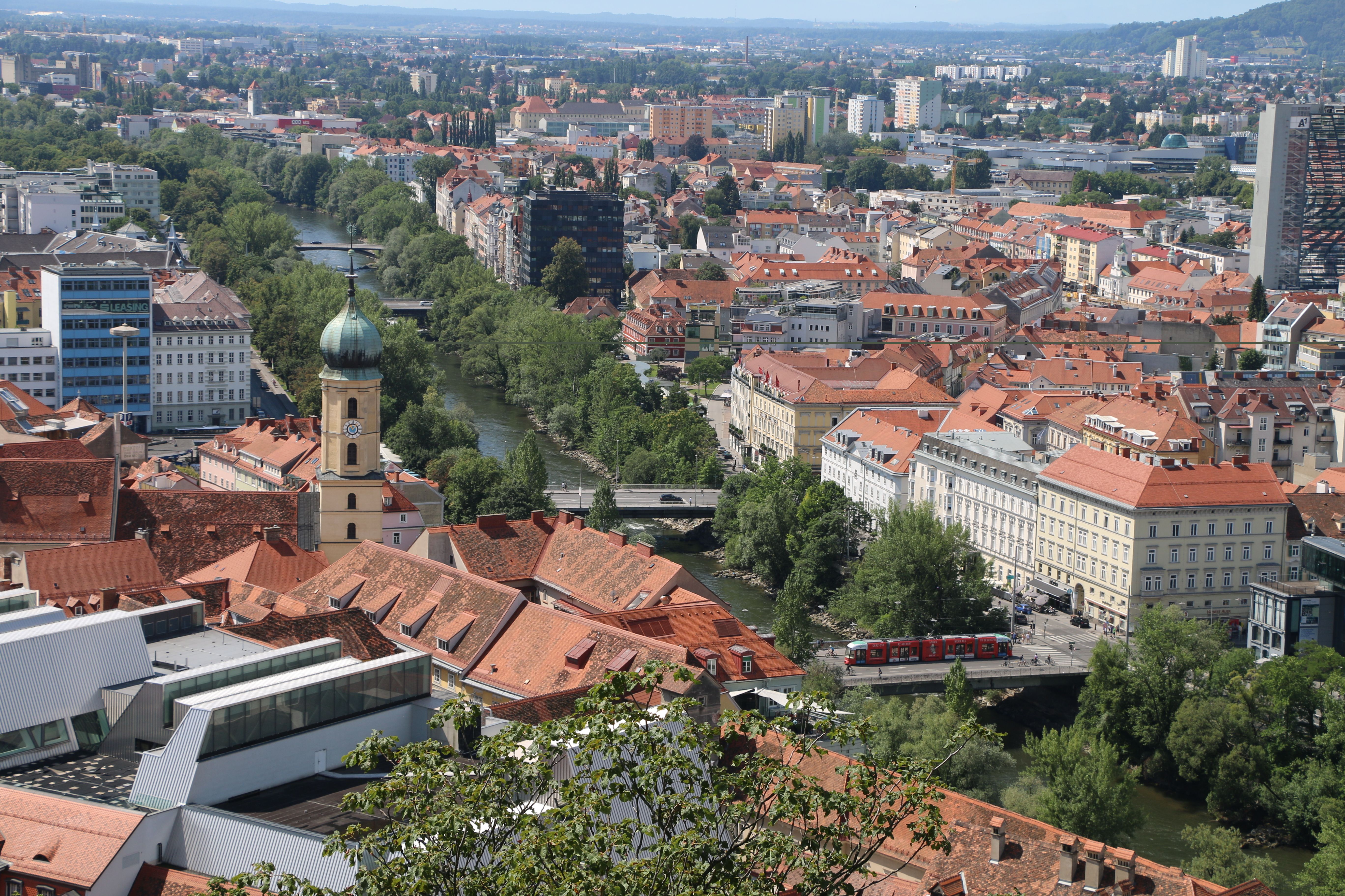 Röda tak i Graz gamla stad, ett kyrktorn och floden Mur sedda uppifrån