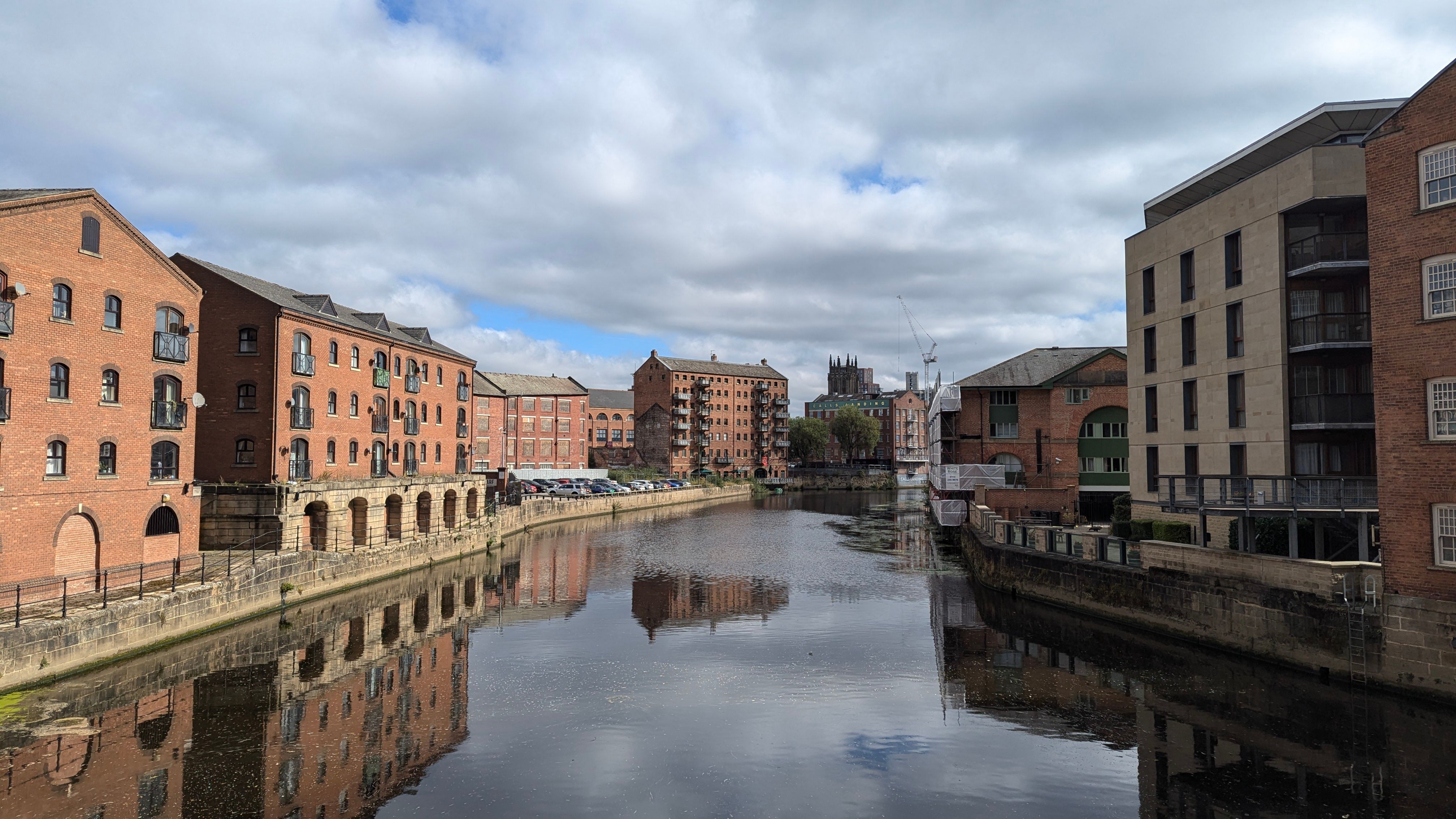 Tegelmagasin och moderna byggnader längs floden i centrala Leeds under en molnig himmel