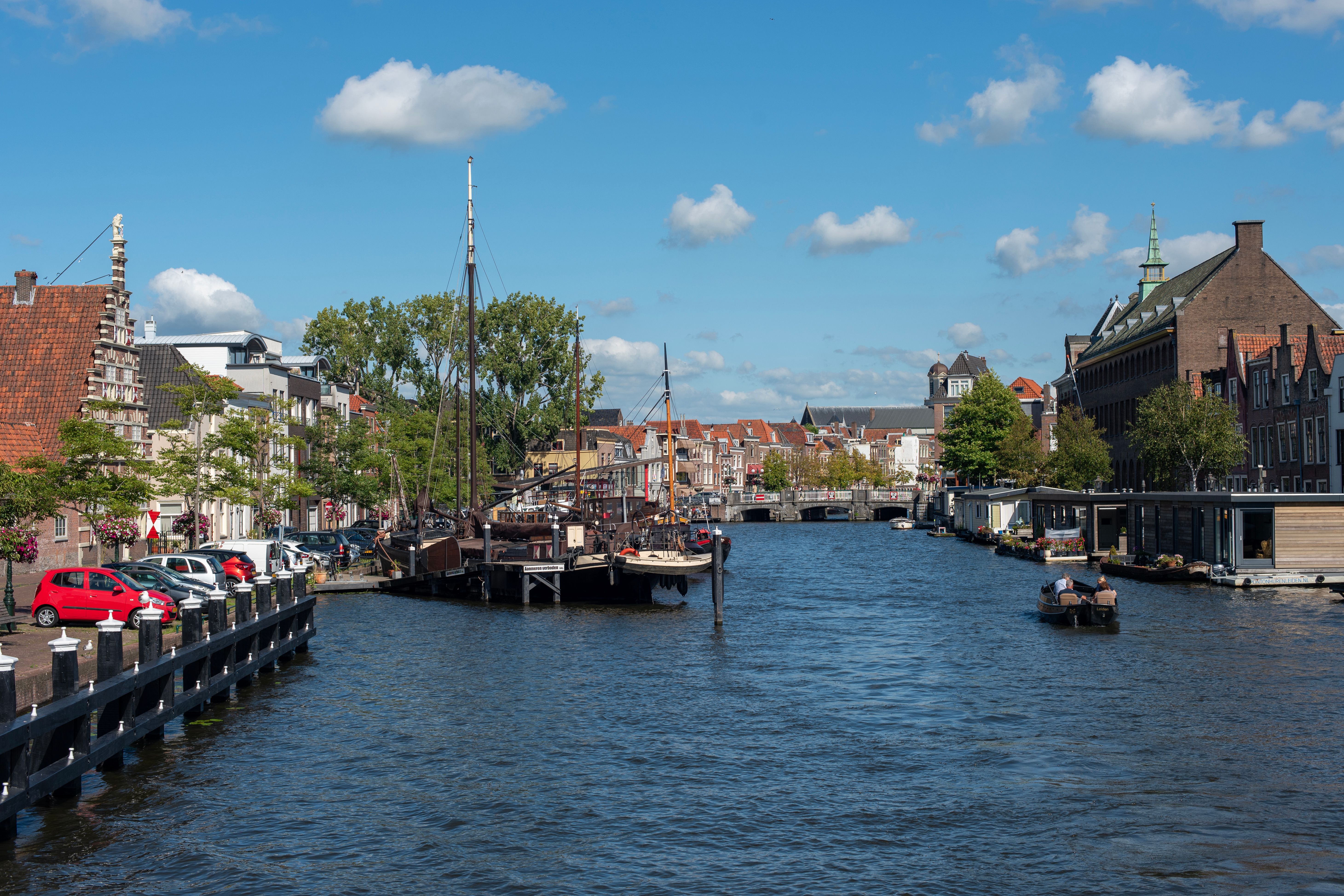 Historic sailing barges moored along a canal lined with old houses in Leiden under a blue summer sky