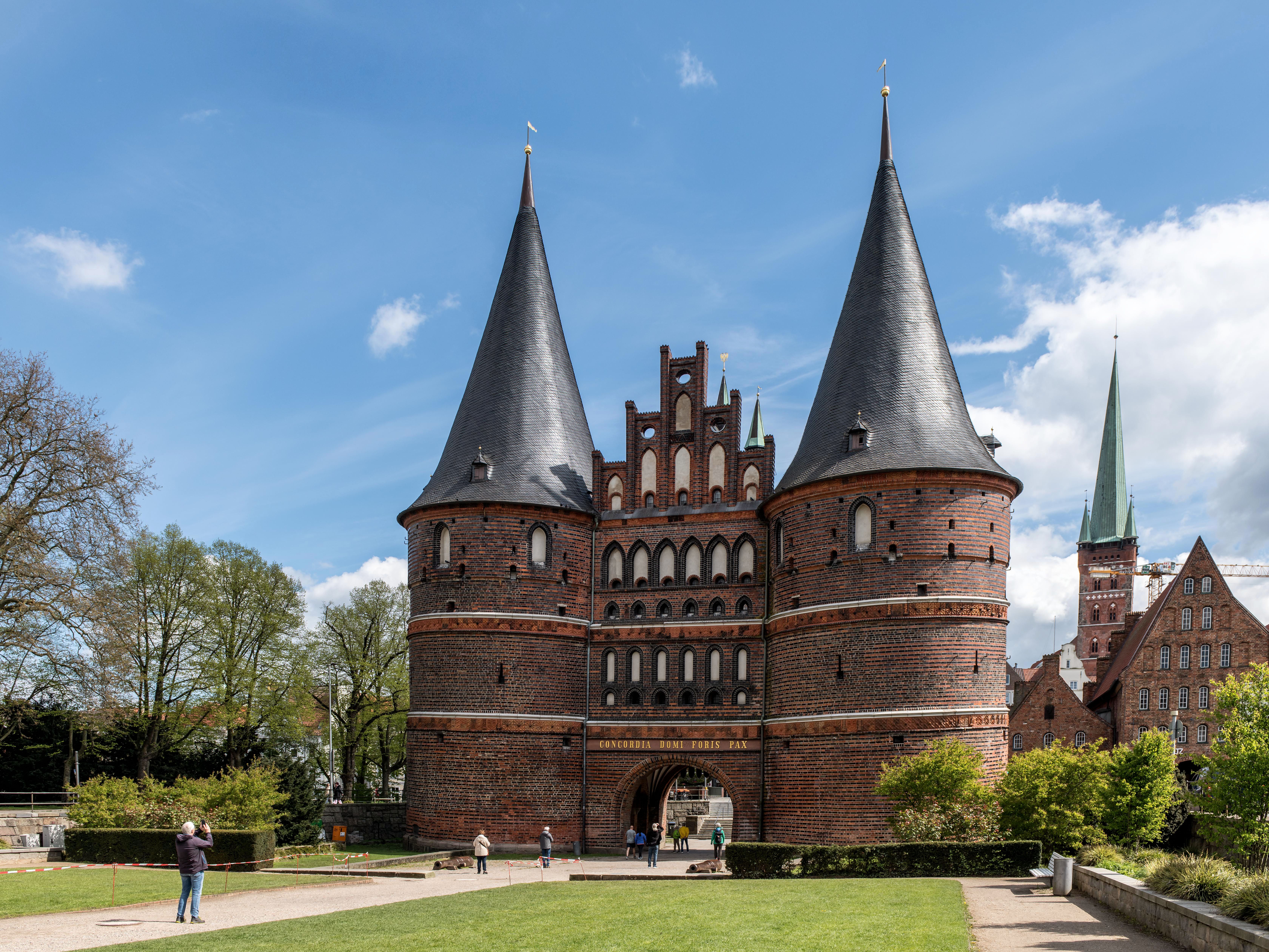 La Holstentor di mattoni con due torri a Lubecca in una giornata di sole, con la guglia della Petrikirche sullo sfondo