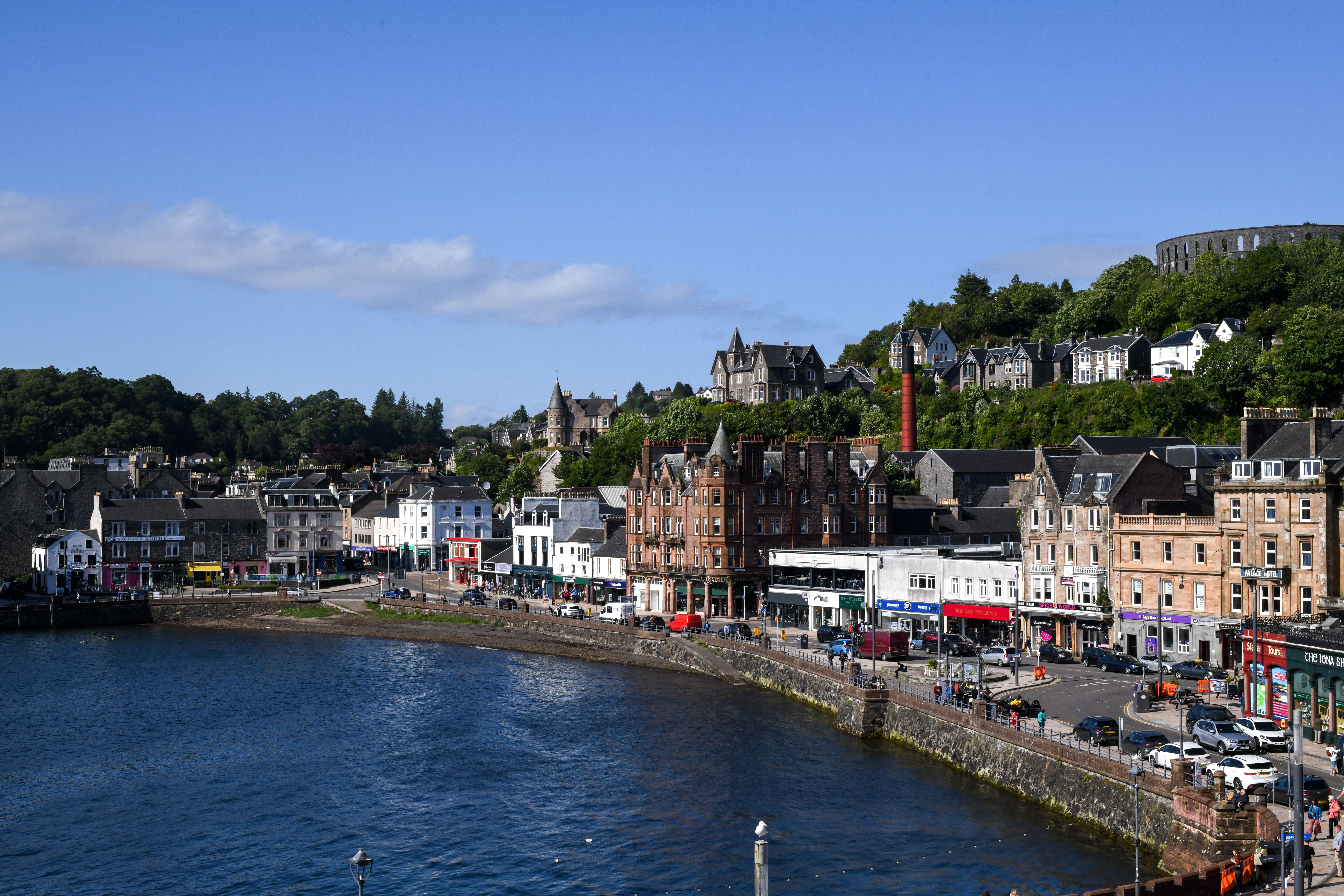 Oban waterfront and bay on a sunny day, with McCaig's Tower on the hill above the town