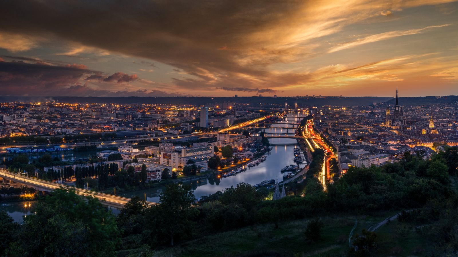 Rouen's Seine river and city skyline at sunset, with the cathedral spire visible.