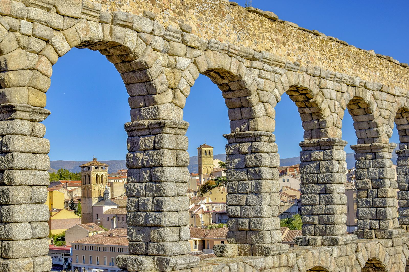 Segovia's Roman aqueduct frames the historic city beneath a clear blue sky.