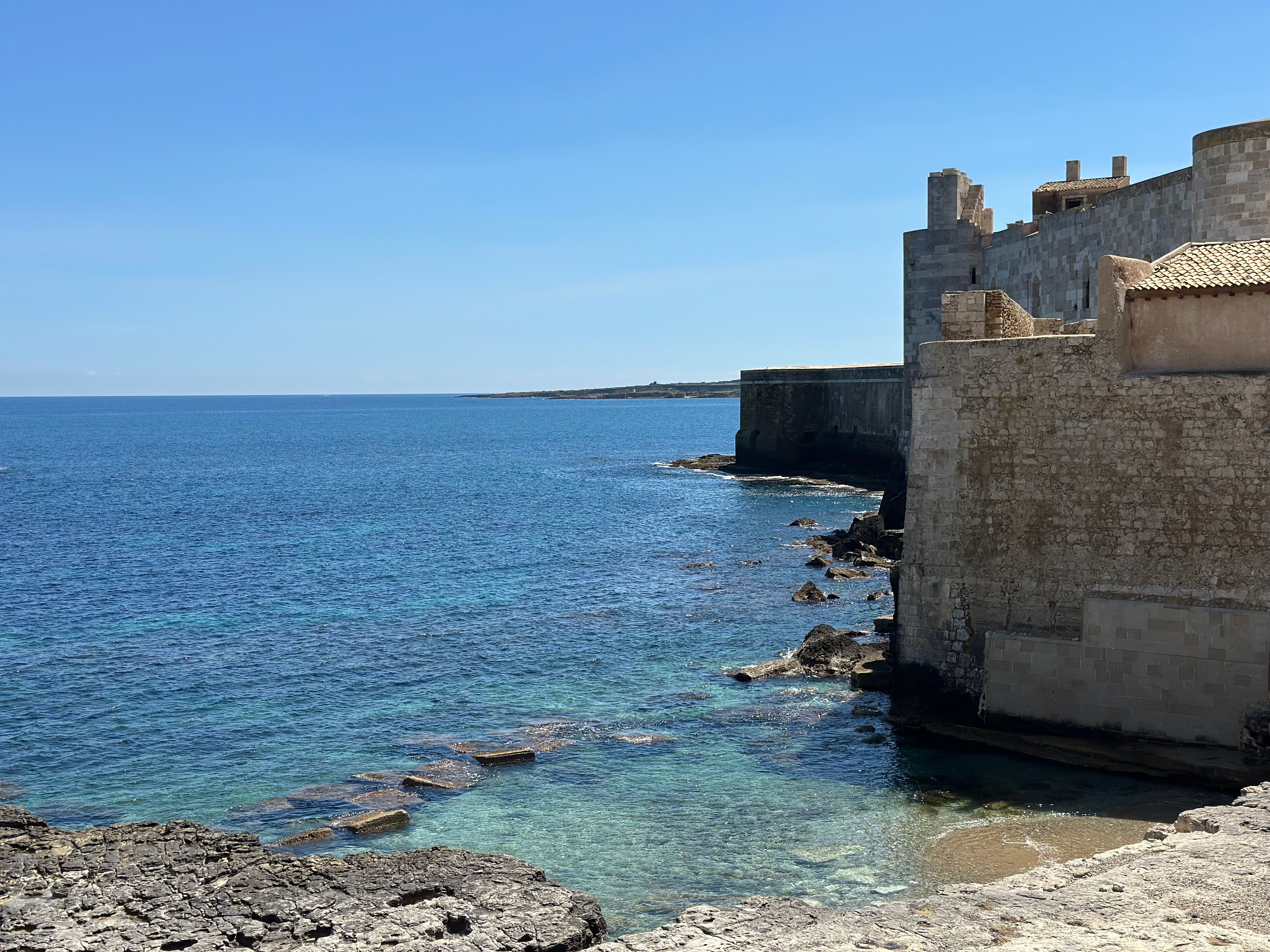 Stone fortifications and clear blue sea on the coast of Ortigia island, Syracuse, Sicily