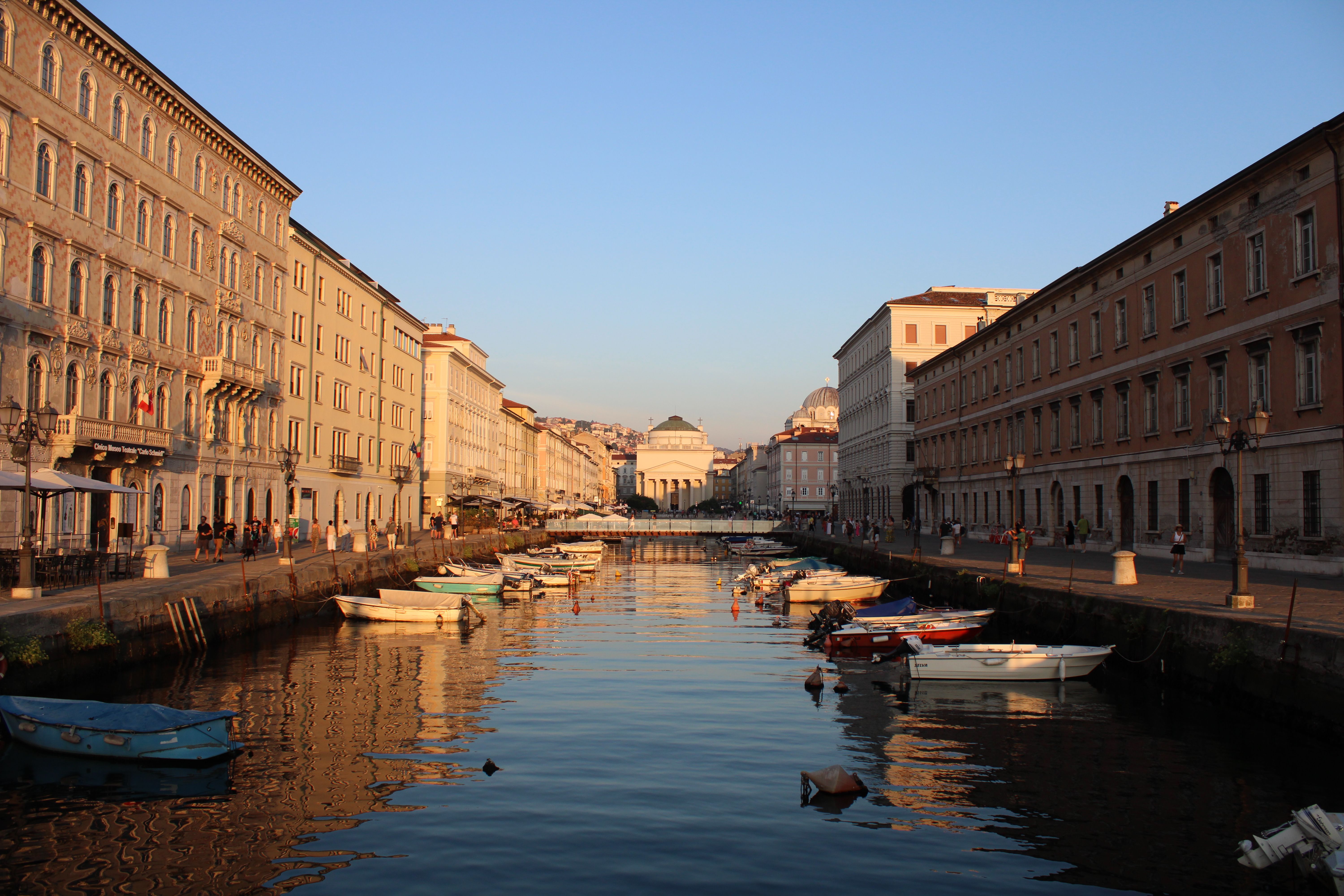 Canal Grande in Trieste at golden hour, boats moored along the water and the church of Sant'Antonio Taumaturgo beyond