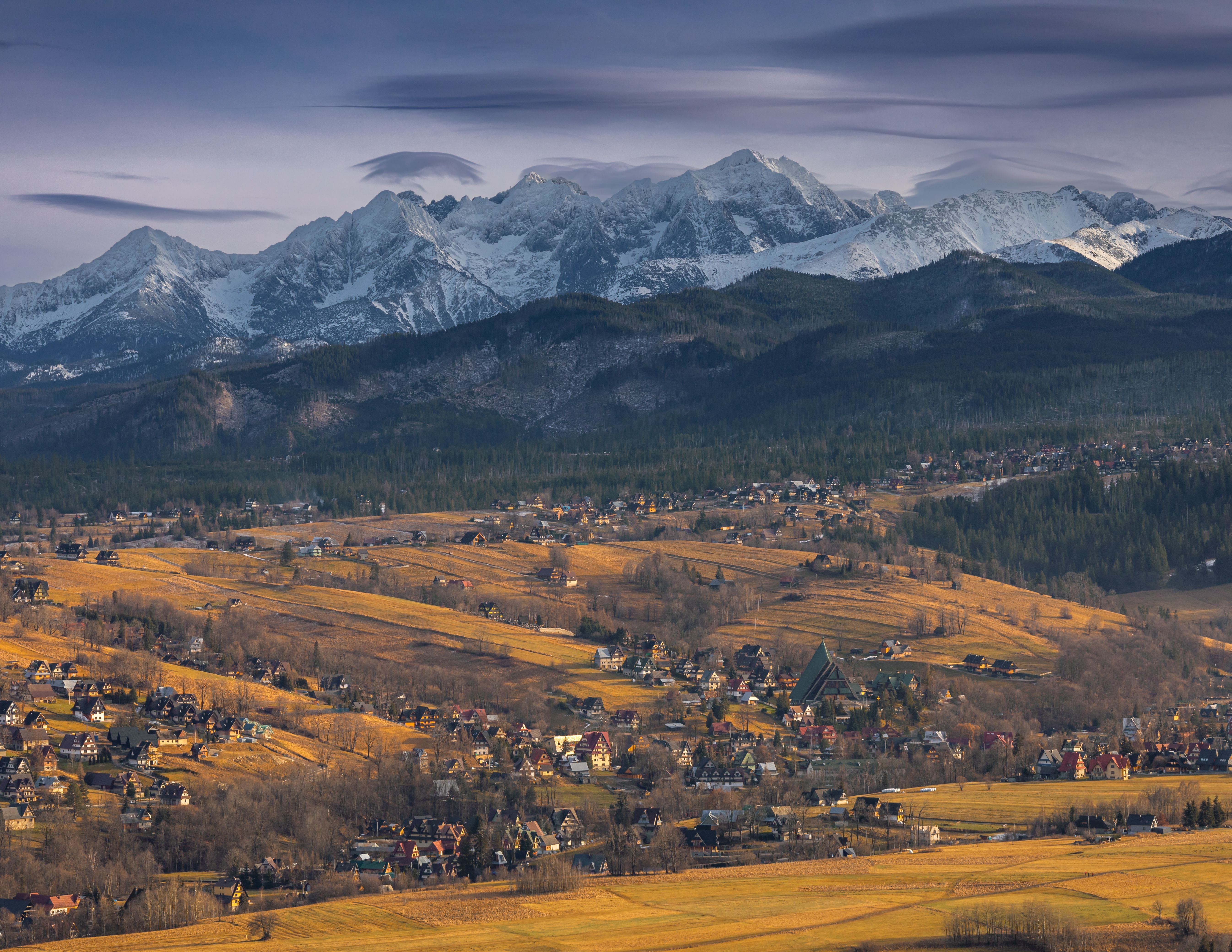 Besneeuwde Tatra-toppen boven houten huizen en herfstweiden bij Zakopane in Polen